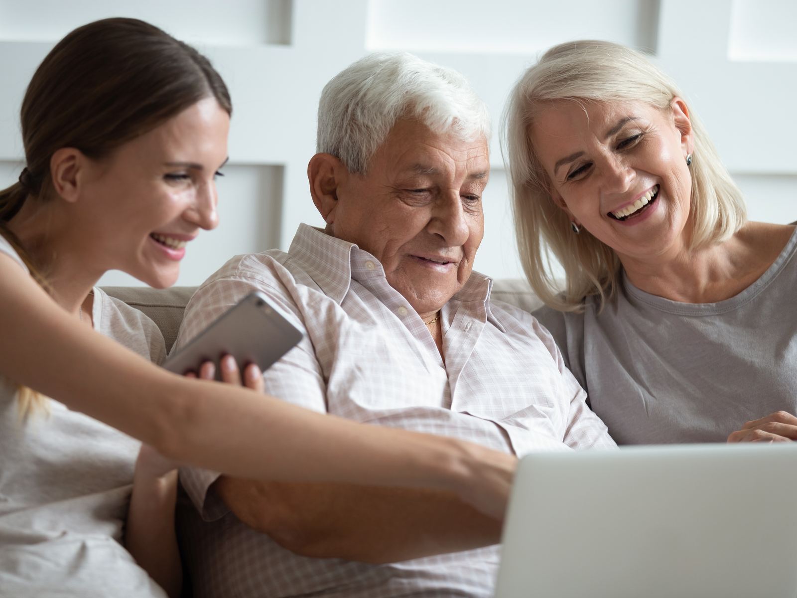 Adult daughter with her elderly parents gathered around a laptop, all smiling and engaged with the screen
